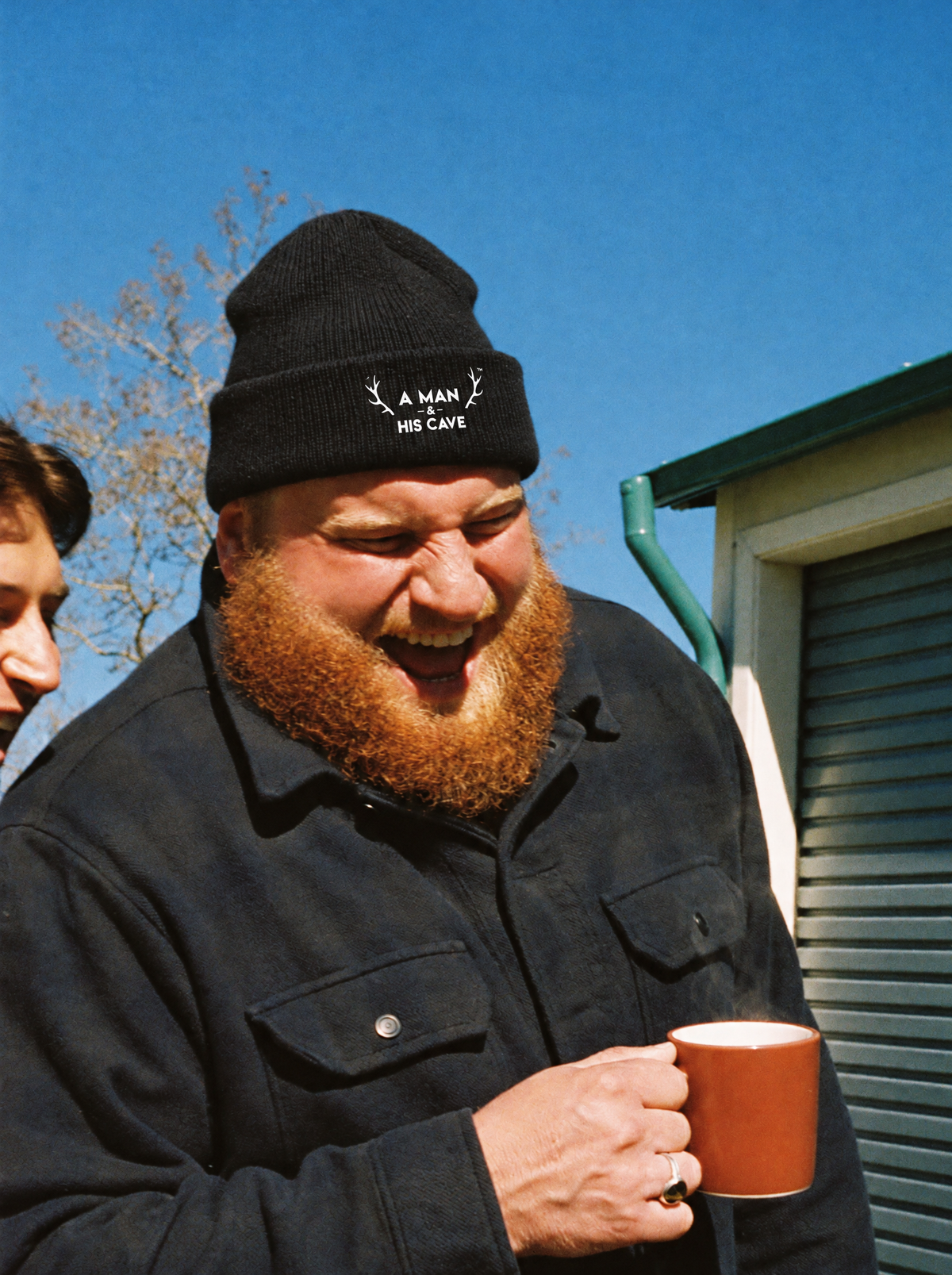 Bearded bloke laughing outside the shed in the black AMAHC logo beanie