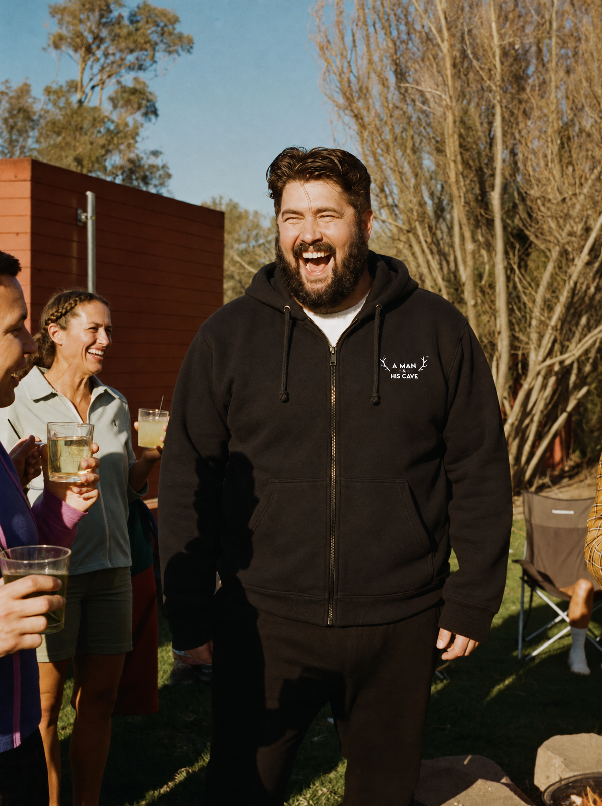 Big bloke laughing by the fire pit in the black AMAHC embroidered zip hoodie