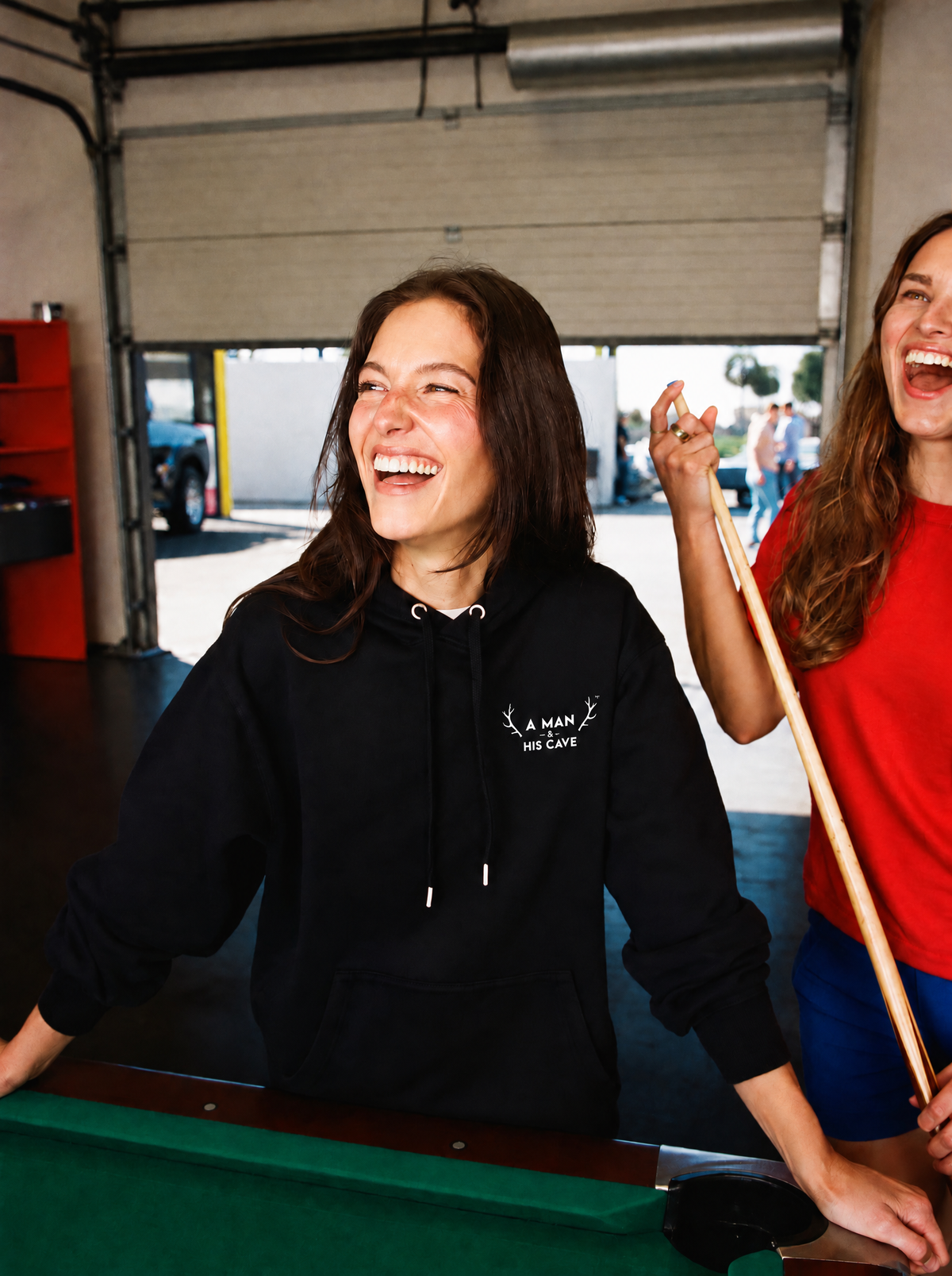 Woman laughing at the pool table in the black AMAHC logo hoodie