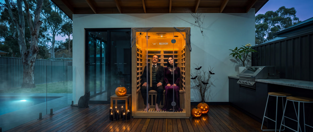 A couple in Halloween costume relaxing in a 2-person infrared sauna on a backyard deck at dusk
