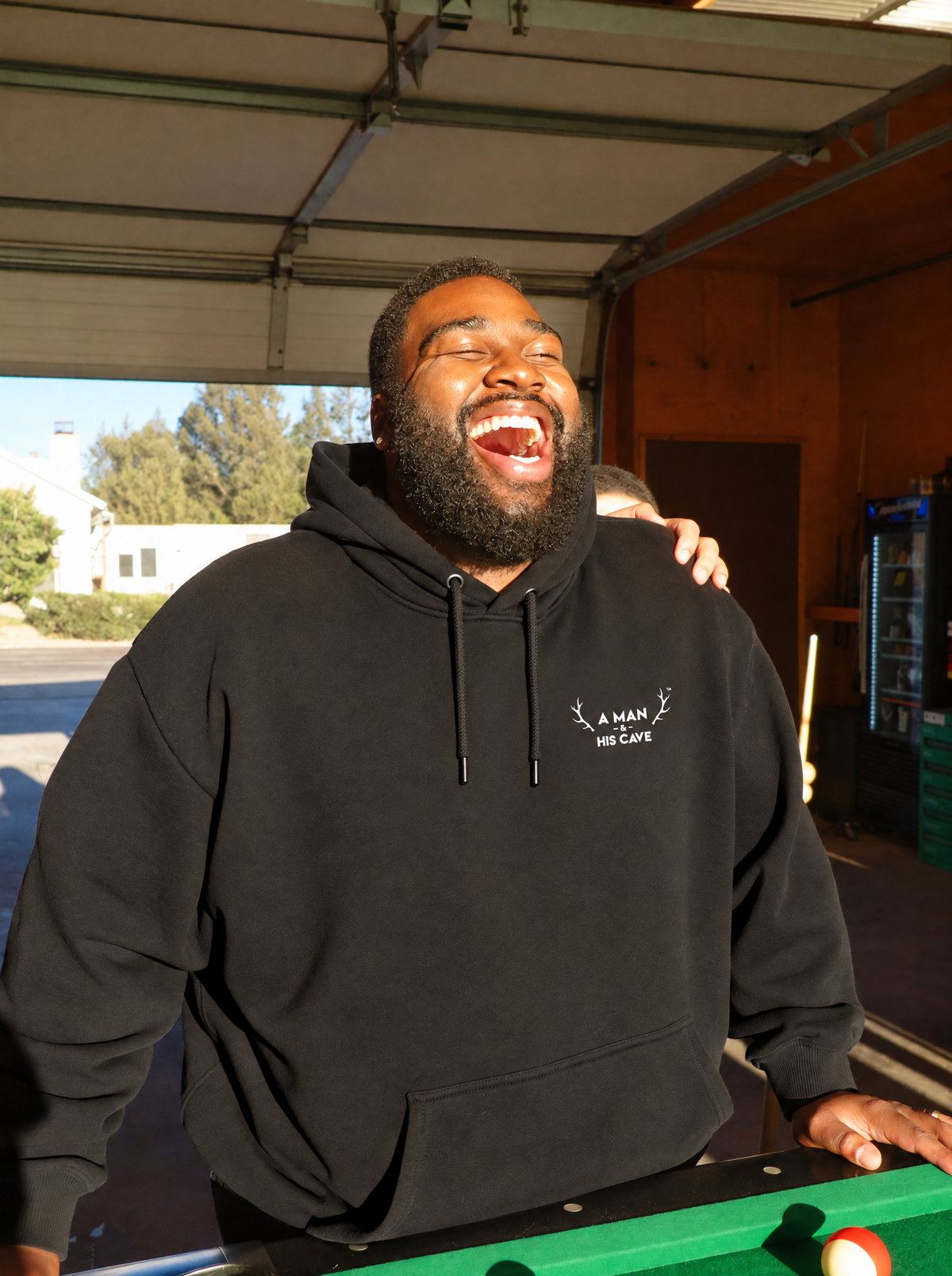 Big bloke laughing at the pool table in the black AMAHC logo hoodie