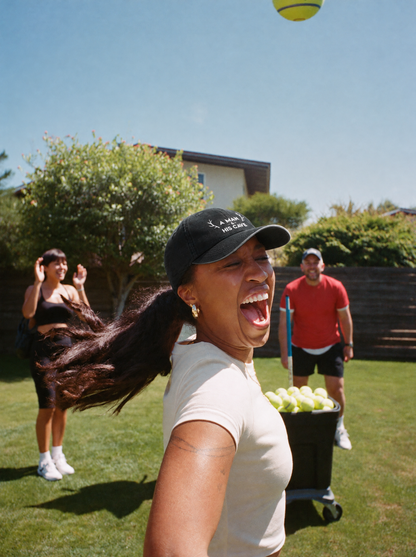 Woman laughing at backyard cricket in the black AMAHC logo dad cap