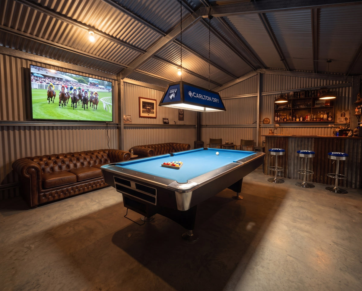 Pool table with a Carlton Dry light in a shed games room with a bar and leather lounges